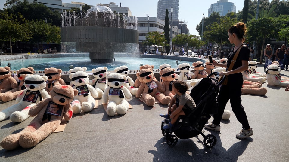 A mother and child in a stroller look at a memorial made of teddy bears blindfolded in Tel Aviv.