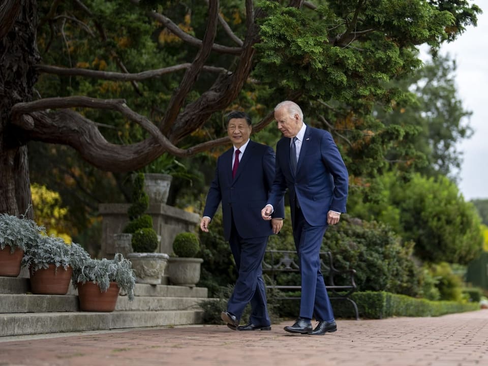 Xi und Biden laufen nebeneinander auf einem Weg durch einen Garten.