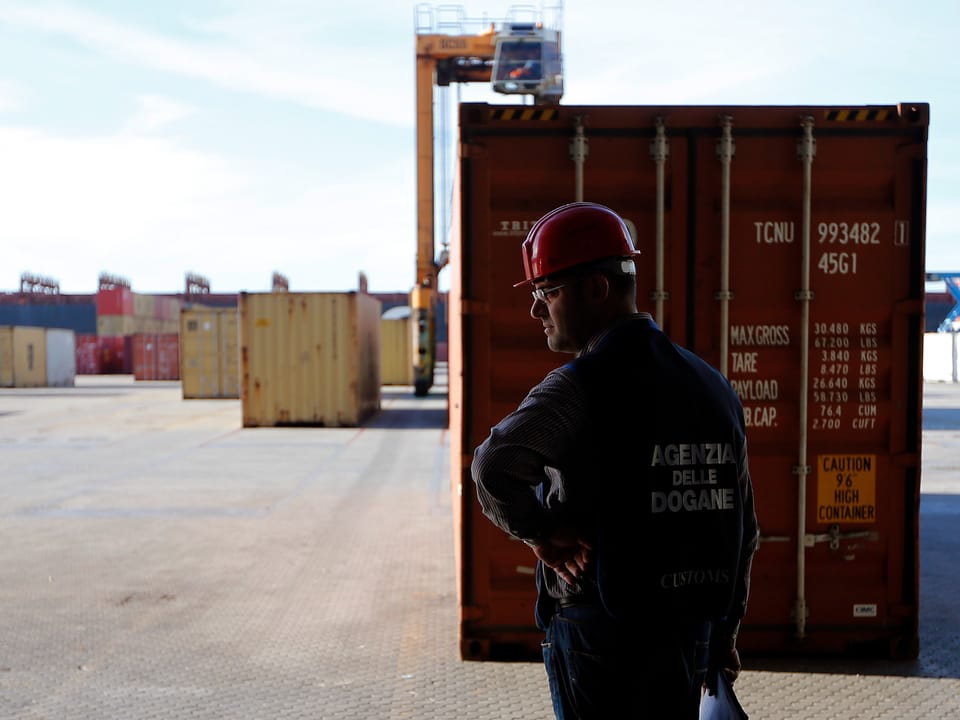 A security guard stands between containers at the port.