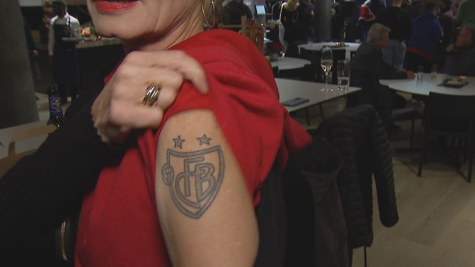 A woman shows her tattooed upper arm with the FCB logo.
