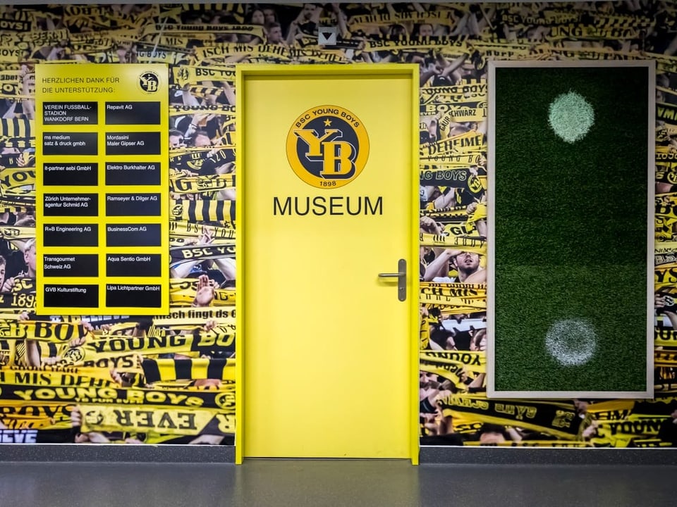 A yellow door with the inscription “YB Museum”.  The wall around the door shows lots of yellow and black YB scarves.