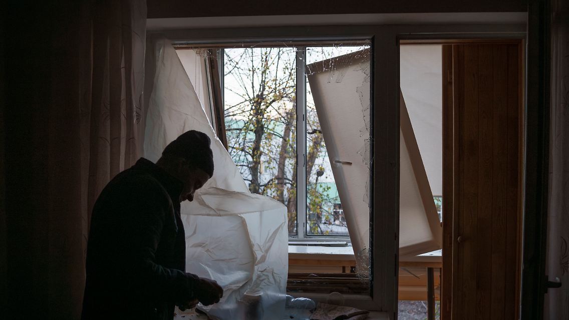 Ein Mann deckt ein zerbrochenes Fenster in seiner Wohnung mit Plastik ab.
