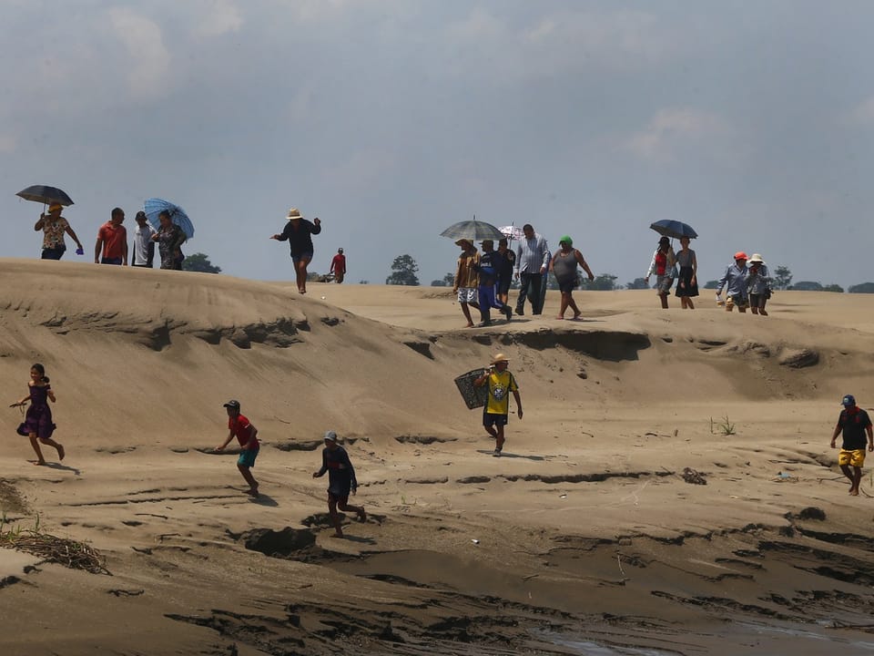 dry dunes, a dozen people walk, some with umbrellas.