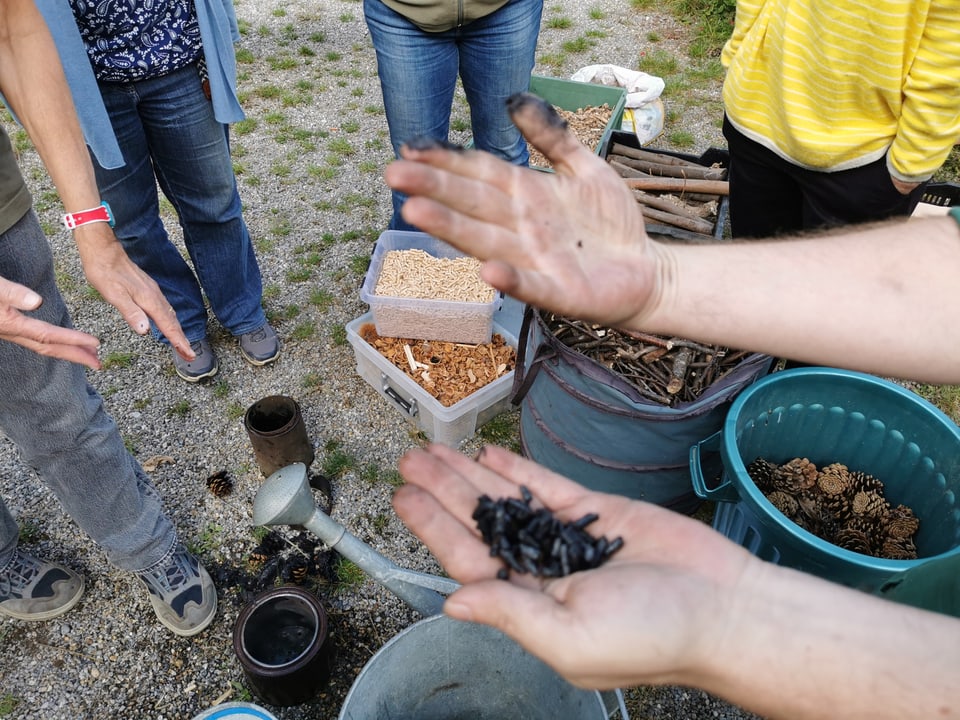 Two hands with black fingers.  The finished biochar lies in the left hand.