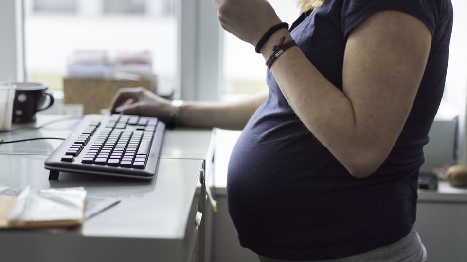 Pregnant woman with belly stands at a desk with a keyboard