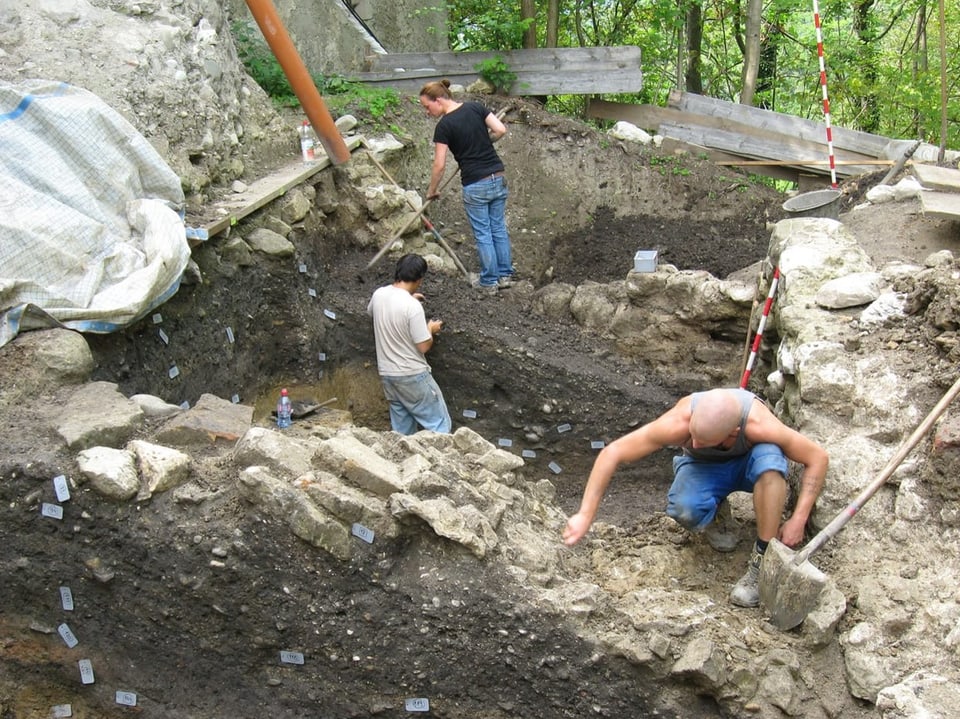 Three specialists stand in a construction pit and examine the earth and rock.