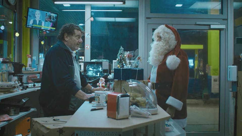 A man and Santa Clause face each other at a counter. 
