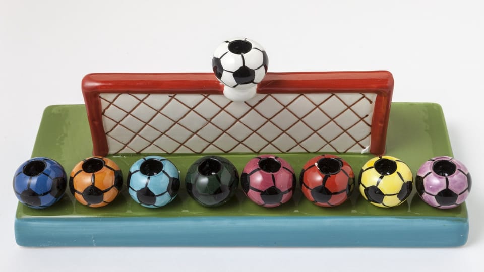 A Hanukkah candlestick, i.e. candle holder with space for eight candles, shaped like a goal and colorful footballs.