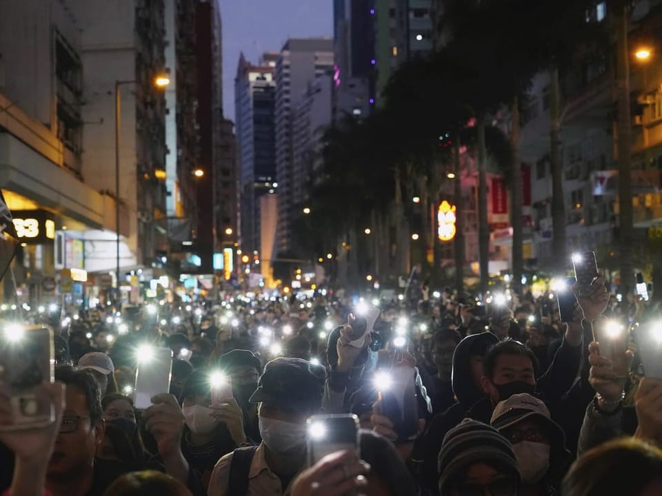 People in the streets light up their cell phone flashlights.