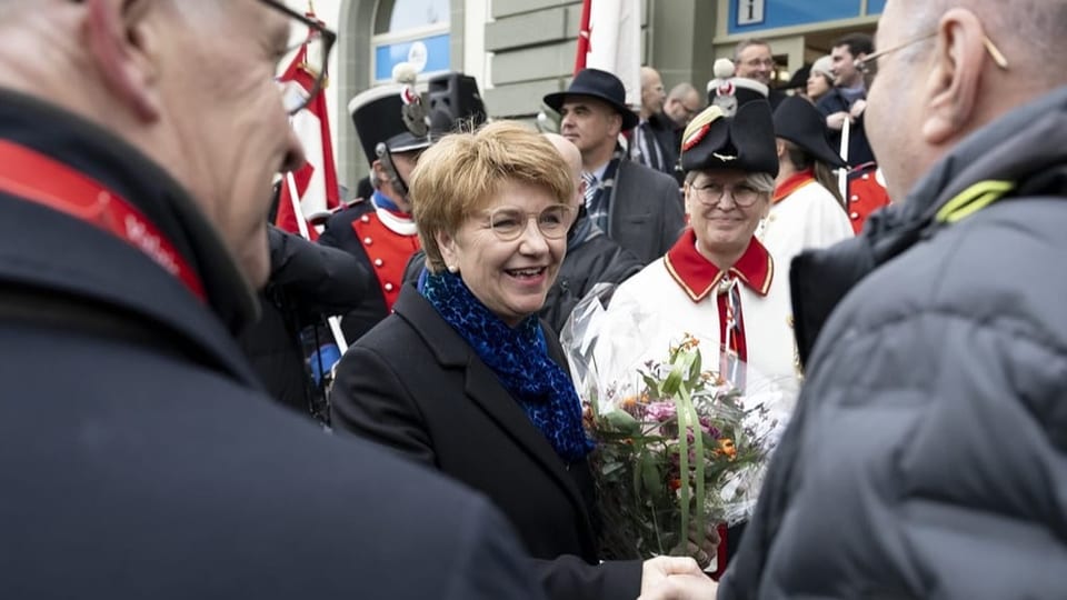 Woman with a bouquet of flowers is greeted in a crowd.