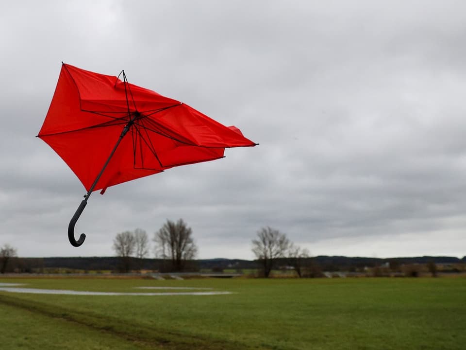 A broken red umbrella in the air.