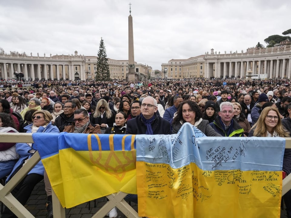 People in the Vatican listen to the Pope's speech in front of two Ukrainian flags.