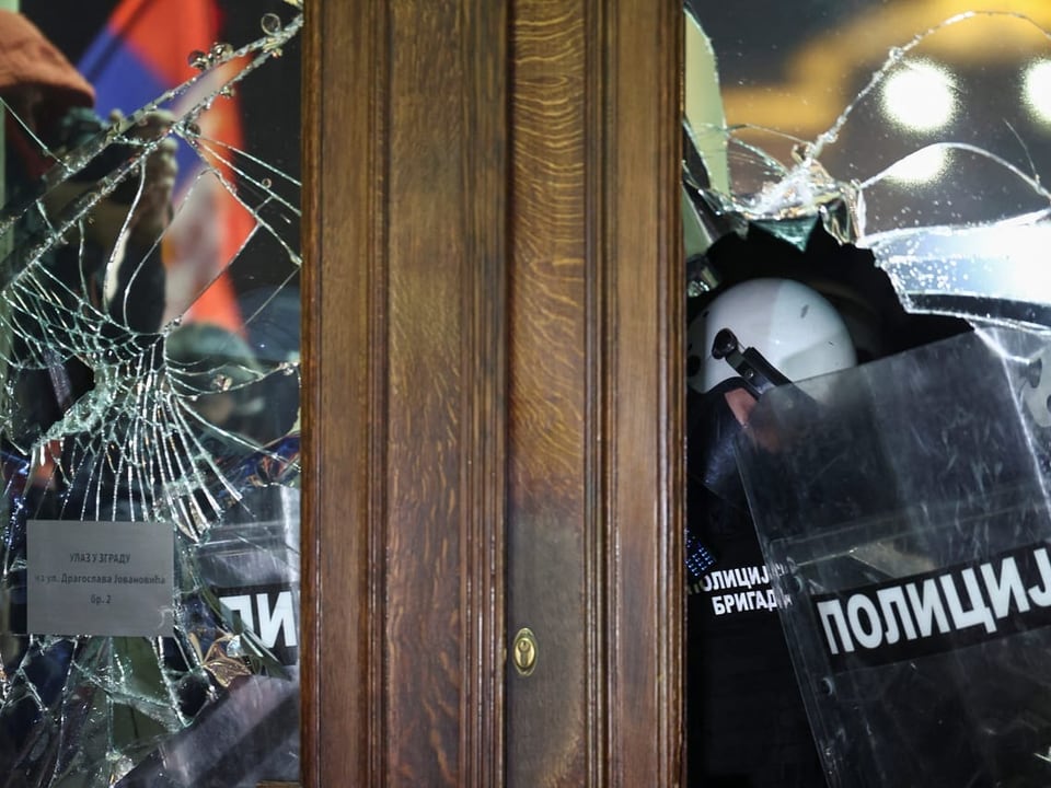 Police officers can be seen behind broken windows in Belgrade City Hall.
