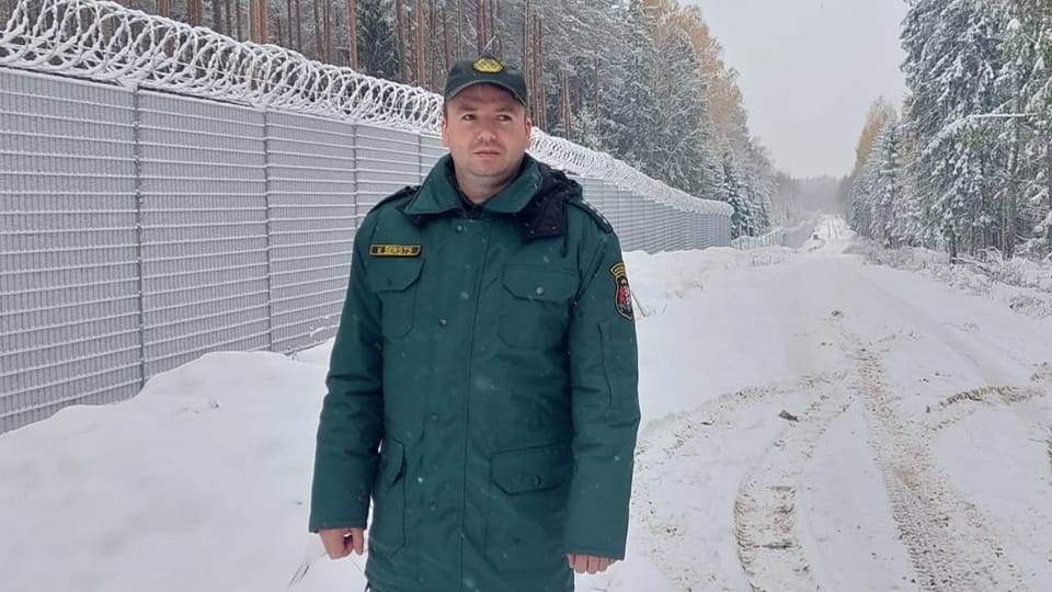 Man in uniform in front of border fence.  It's all snowy.