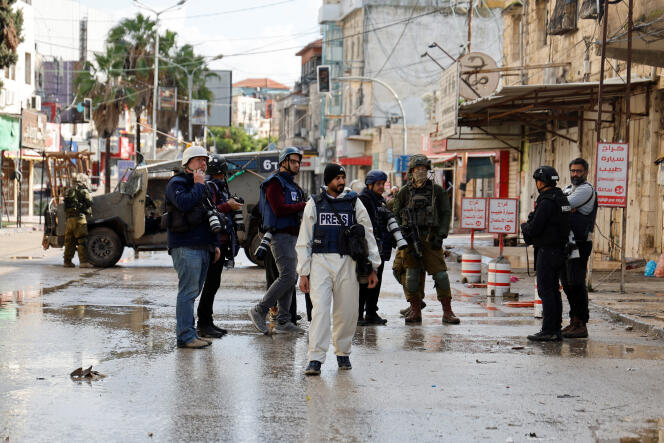 Journalists gather as Israeli military vehicles block the road during a raid in Jenin, part of the ongoing conflict between Israel and the Palestinian Islamist group Hamas, in the Israeli-occupied West Bank, December 13, 2023. 