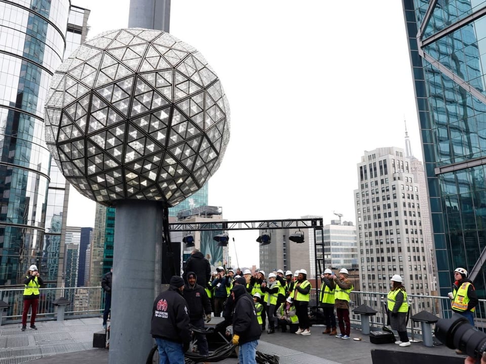 People in fluorescent vests stand in front of the large ball that descends at the turn of the year.