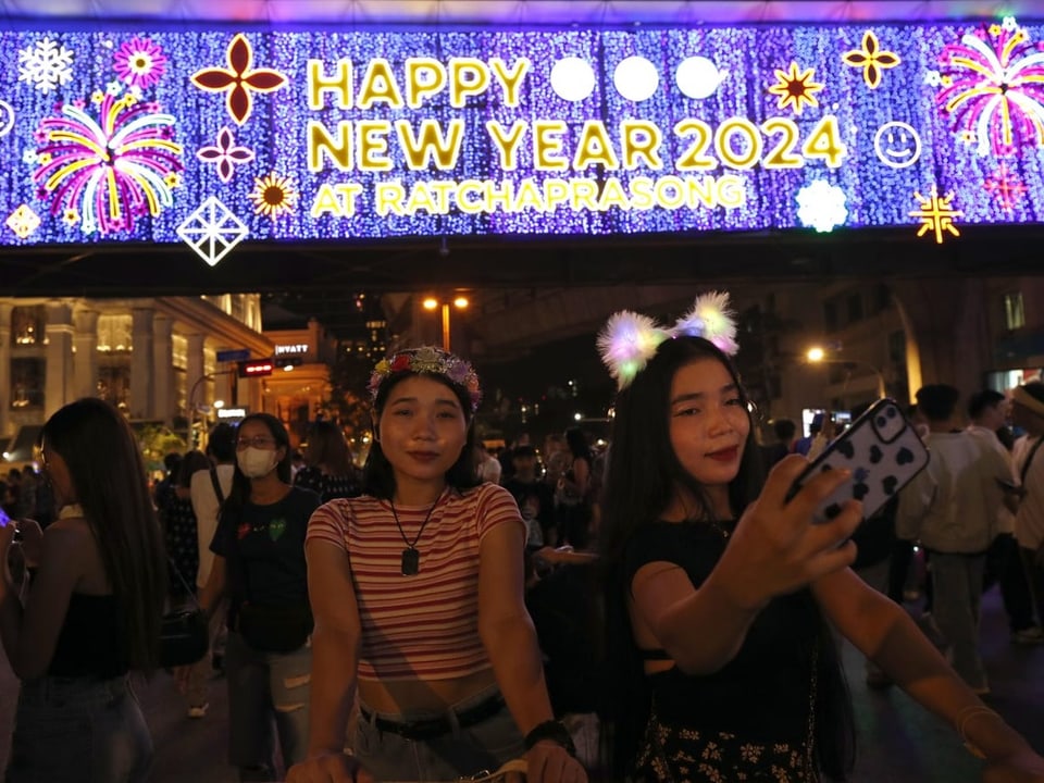 Two women stand in front of an illuminated sign with New Year's wishes and take a selfie.