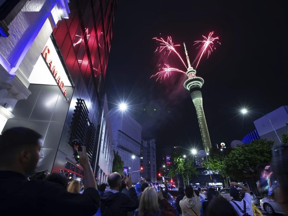 People on the street look up at the tower.  Fireworks light up above.