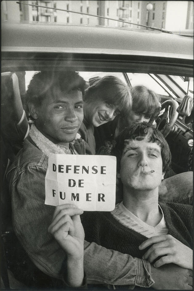 “Young people smoking in a car and holding a “No smoking” sign”, Carros, April 1983.