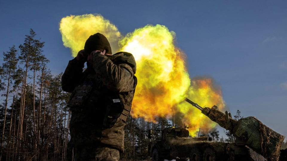 Artillery fires, a soldier covers his ears.