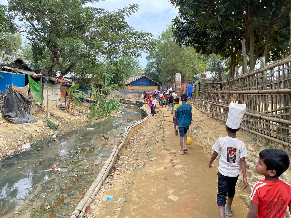People walk on a path along the polluted stream.