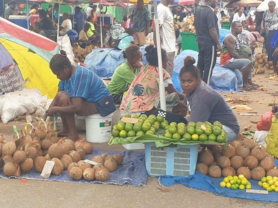 Market scene.  Fruits are offered on cloths on the ground, but it is not abundant.