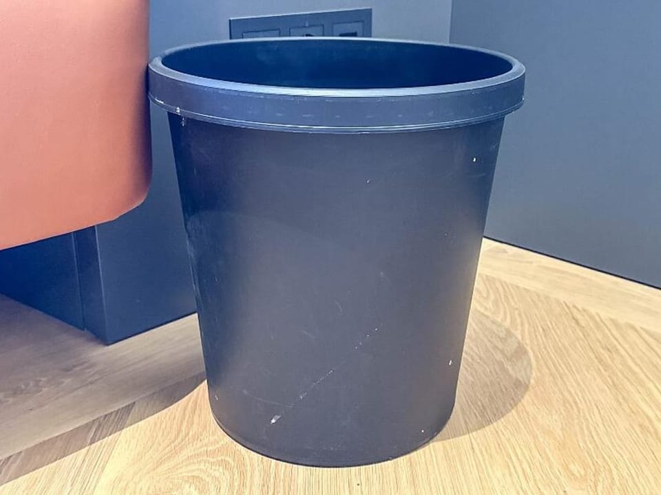 A blue plastic trash can sits on a wooden floor