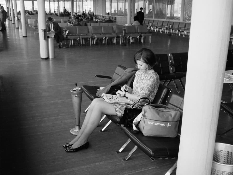 A woman at the airport with a Swissair bag.  The image is black and white.