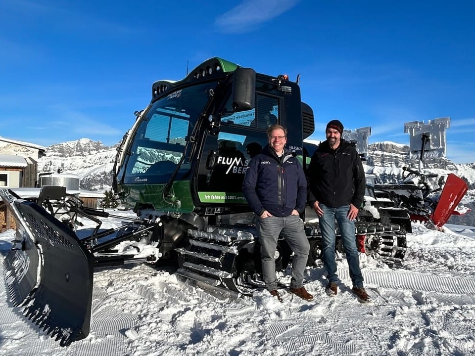 Two people in front of a snow groomer