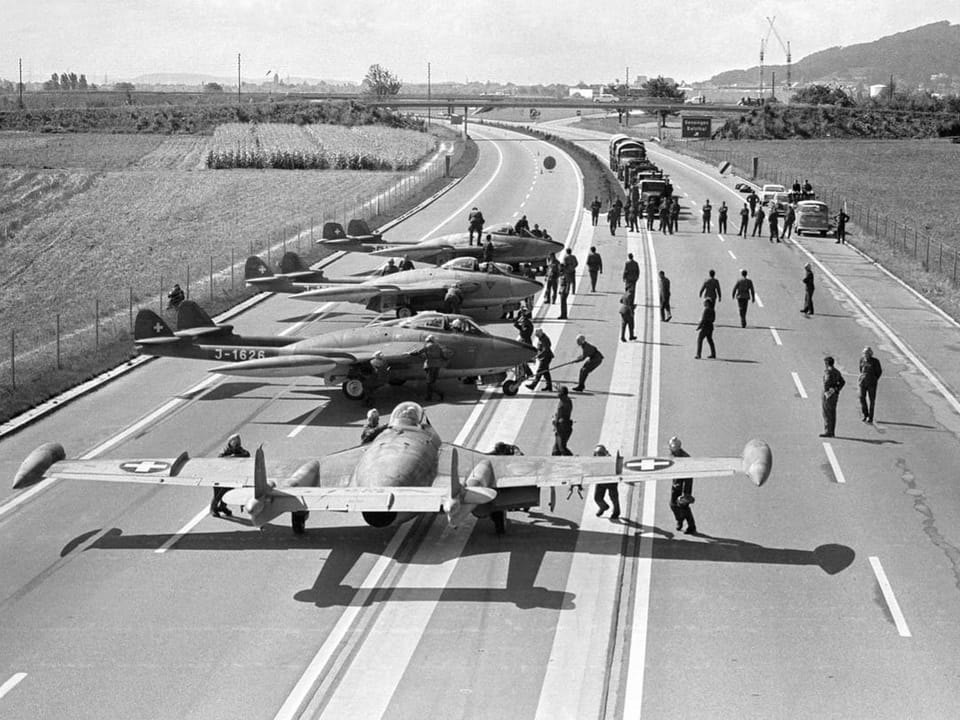 Several fighter jets are parked on a highway;  surrounded by people