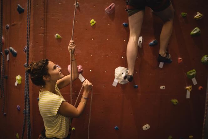 In a climbing gym, a woman belays a climber. 