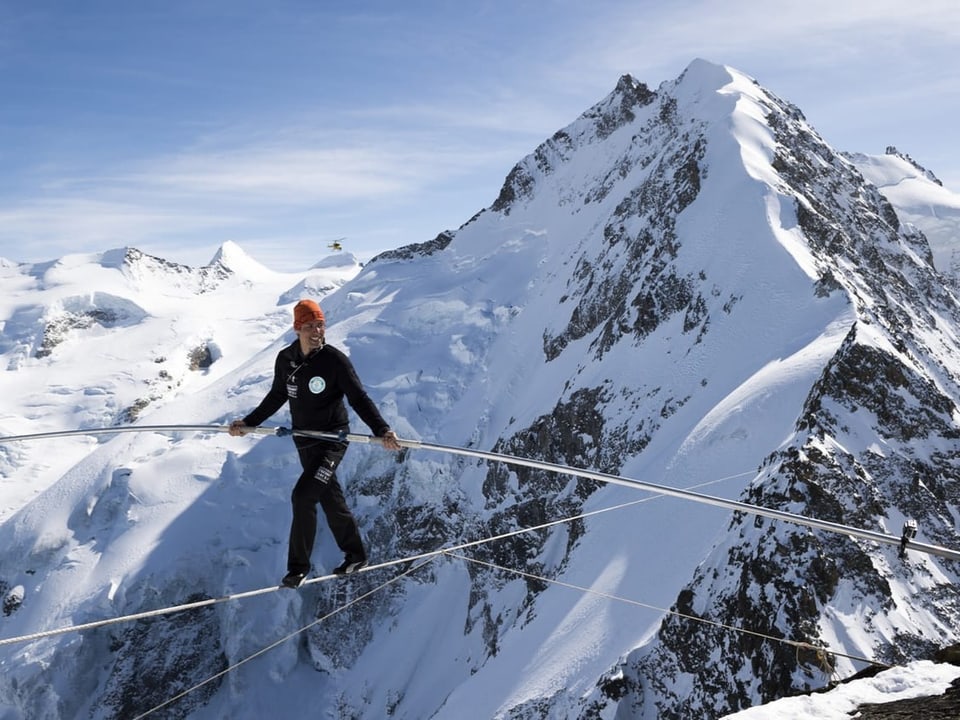 Nock walks over a high rope in front of an alpine mountain panorama.
