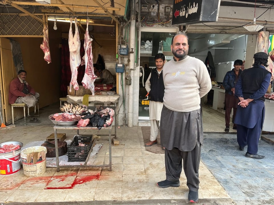 Man stands in front of a butcher's stand.