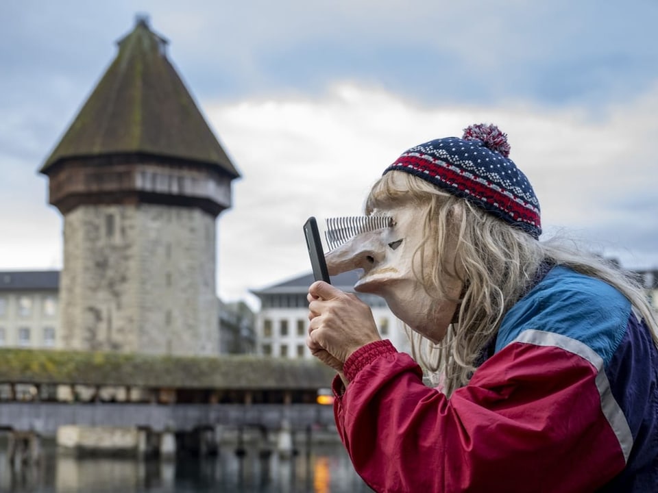 A disguised person with a mask stands in front of the water tower in Lucerne.  He fixes his eyes on the cell phone.