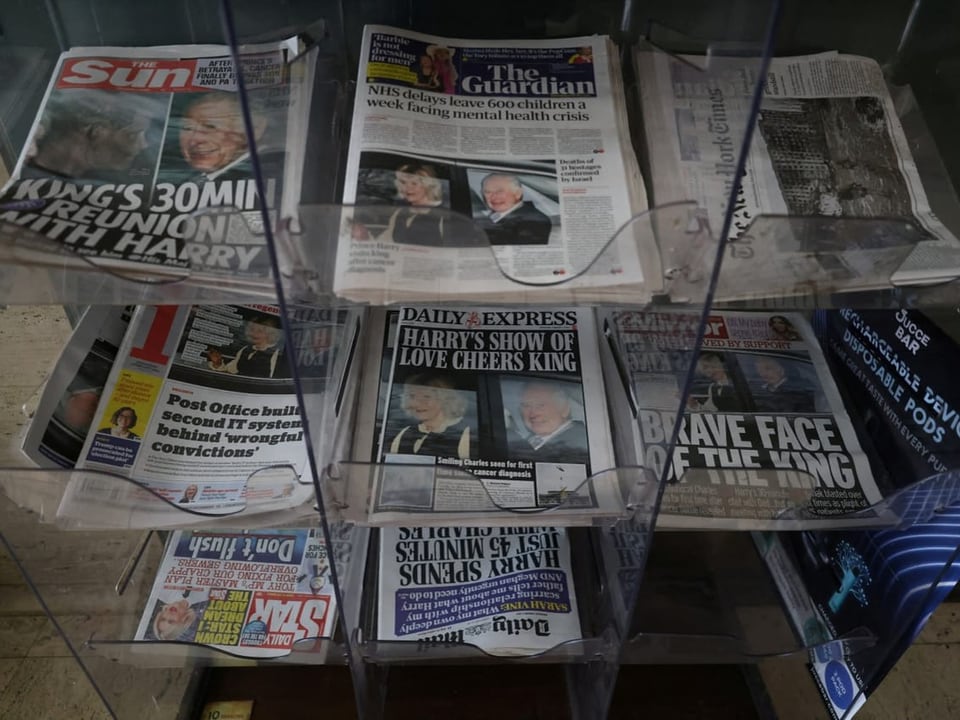 Various newspapers are on a shelf.  Everyone has the same news on the front page.