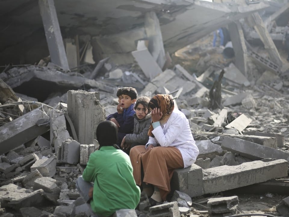 A woman and three children sit in the rubble in Rafah.