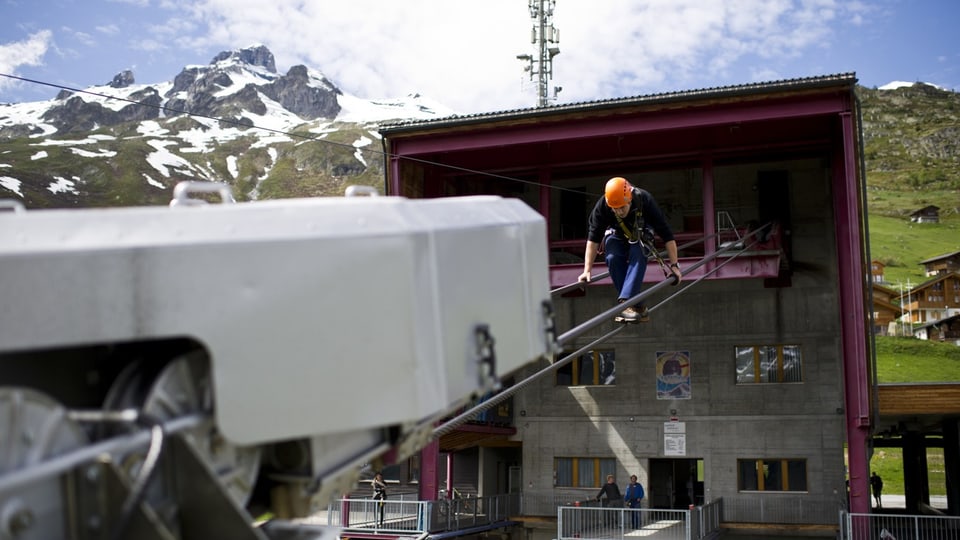 Man with a construction helmet at the mountain station of a cable car.  He walks on the tightrope.