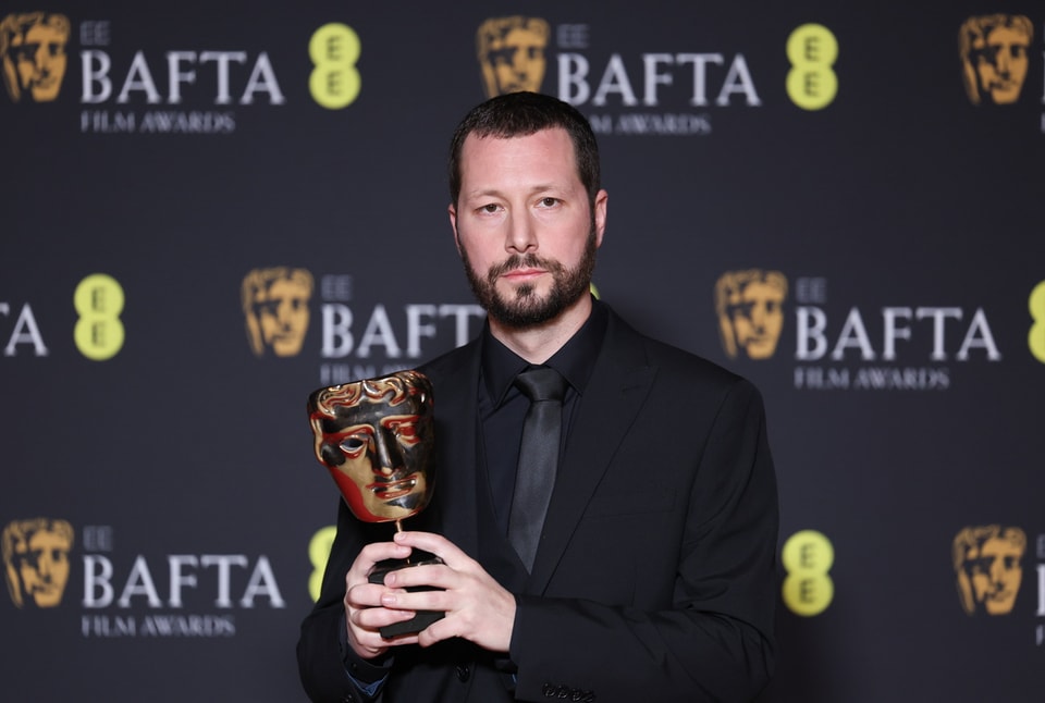   Mstyslav Chernovs in front of the Bafta wall with a trophy in his hand.