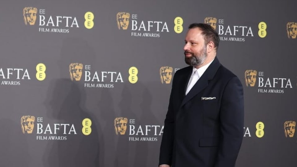   Yorgos Lanthimos in side profile in front of the Bafta wall.