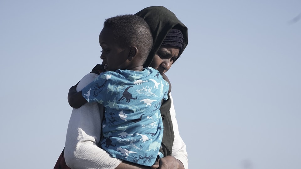 A Sudanese evacuee carries her son.