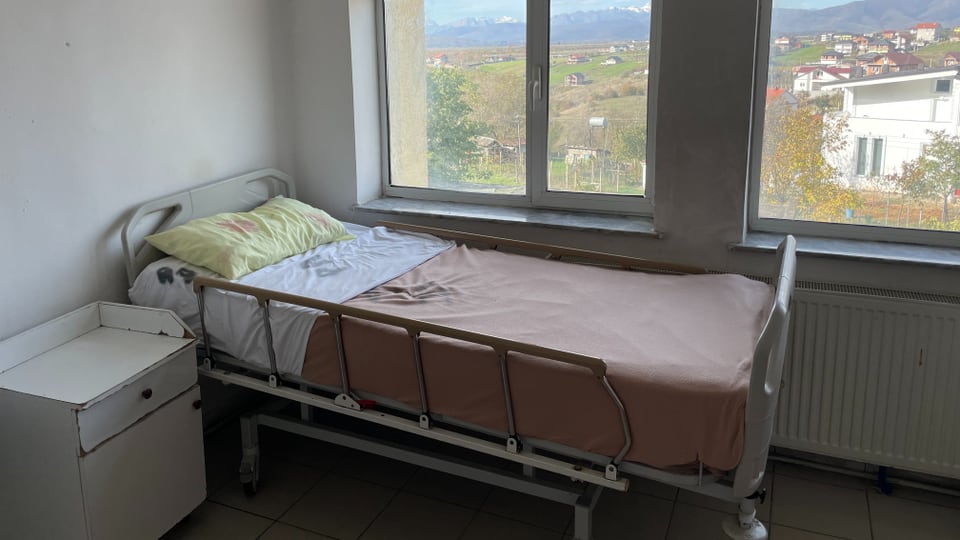 An empty hospital bed behind it the mountains of Kukes
