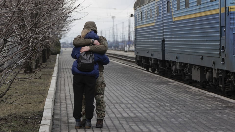 A woman hugs her husband at a train station. 