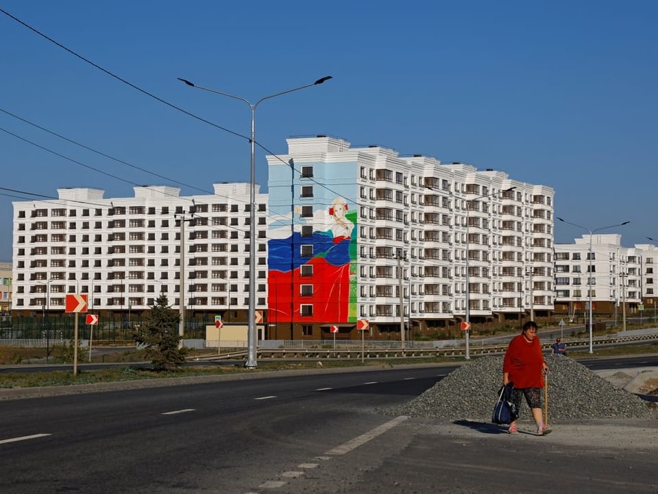 A woman walks near the newly built apartment blocks.  Russian flag on white building.