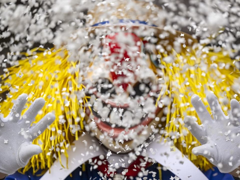 A person wearing a costume and mask throws confetti into the camera.