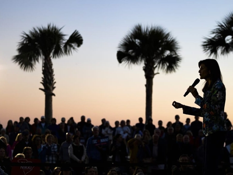 Nikki Haley, voters and palm trees appear in the backlight.  In the background: the sky in the twilight.