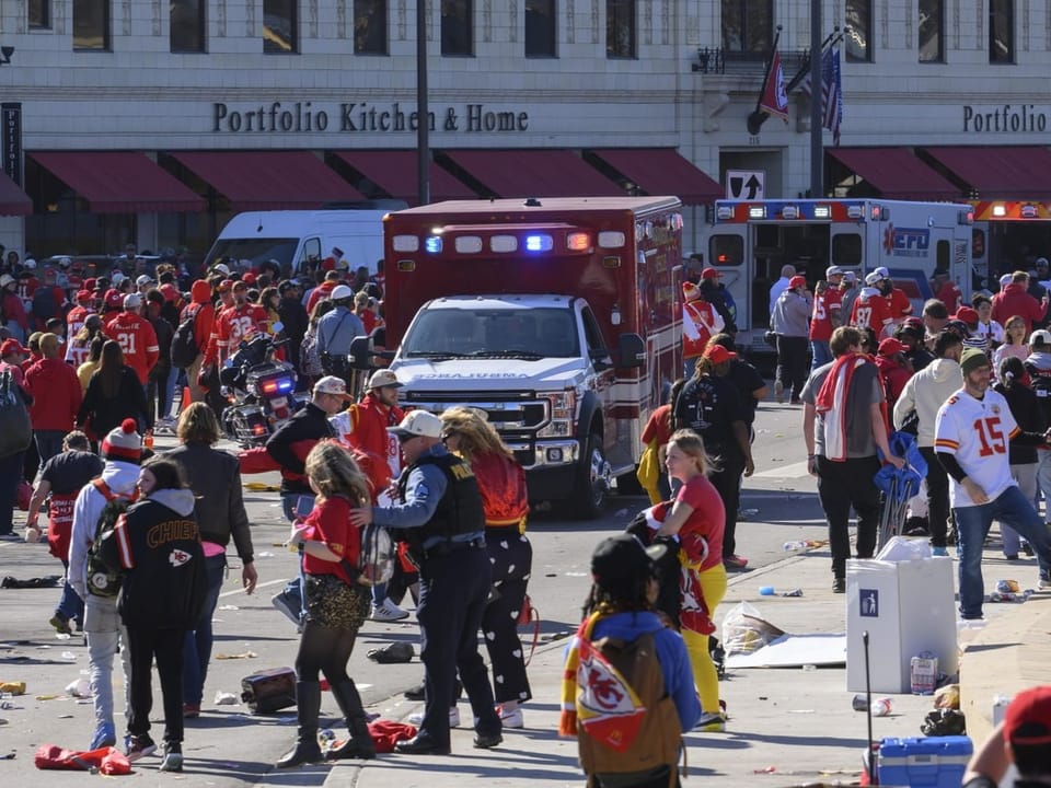 View of a street in Kansas City.  In the foreground people rush away.  Ambulances are waiting in the background.