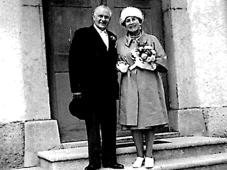 A man and a woman pose for the camera in front of a building.  Old heavy-duty white photo.