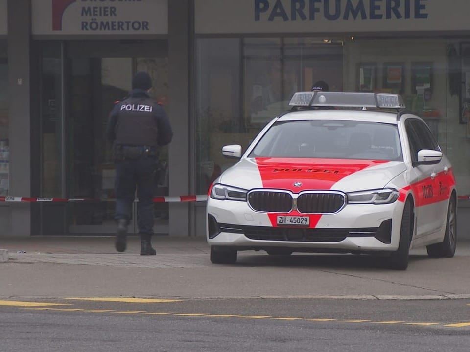 A police car is parked in front of a shop.  A police officer is standing next to him.