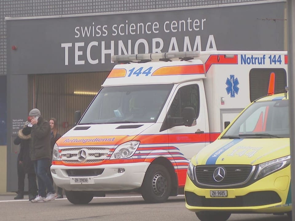 A medical van is in front of the Technorama entrance.  People are standing nearby.