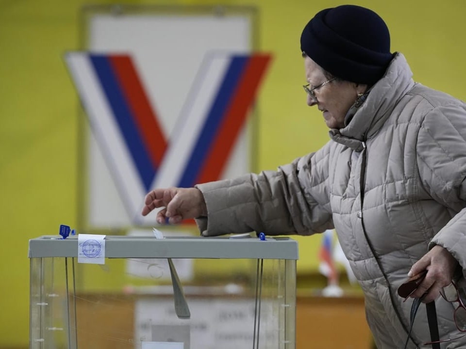 A woman casts her vote into a transparent urn at a polling station